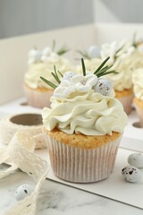 Tasty Easter cupcakes with vanilla cream on white marble table