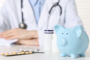 Doctor with piggy bank and pills at white table, closeup