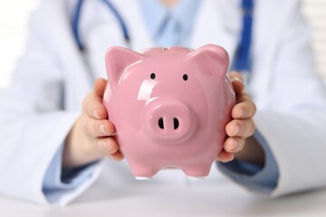 Doctor with piggy bank at white table, closeup