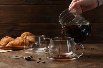 Woman pouring coffee into glass cup at wooden table, closeup
