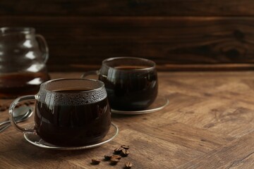 Hot coffee in glass cups and beans on wooden table, closeup. Space for text