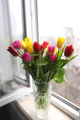 A bouquet of tulips in a vase on the window.