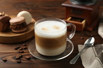 Aromatic coffee in cup, beans, spoon and macarons on wooden table