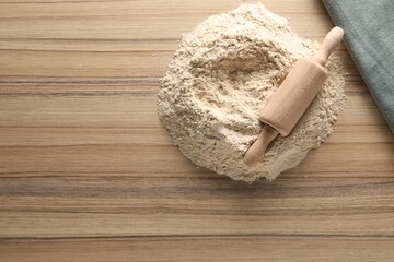 Pile of flour and rolling pin on wooden table, top view. Space for text