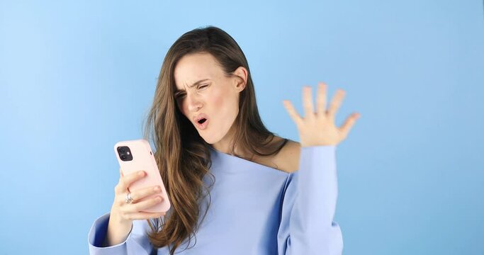 Online conflict. Negative video call. Boomerang animation. Virtual quarrel. Furious unhappy comic woman yelling swearing on phone camera standing isolated on blue background.