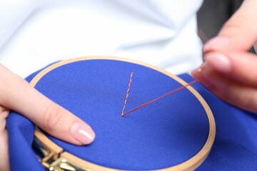 Woman with sewing needle and thread embroidering on cloth, closeup