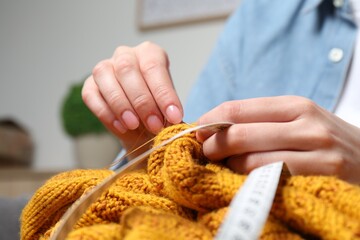 Woman sewing sweater with needle at home, closeup