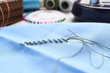 Light blue cloth with sewing needle, thread and stitches on table, closeup