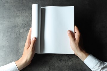 Man holding blank notebook at black textured table, top view. Mockup for design