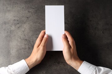 Man holding blank card at black textured table, top view. Mockup for design