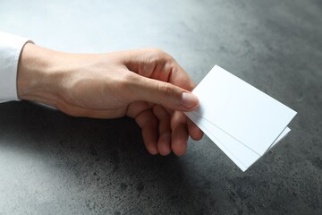 Man holding blank cards at black textured table, closeup. Mockup for design