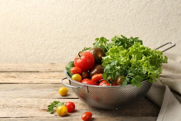 Wet vegetables in colander on wooden table, closeup. Space for text