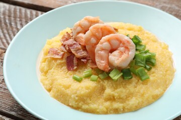 Plate with fresh tasty shrimps, bacon, grits and green onion on wooden table, closeup