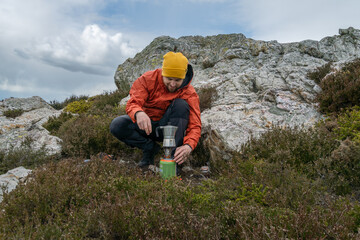 Fototapeta premium Making coffee with portable gas stove in nature, hiker takes a break after a long walk.