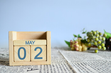 May 2, Calendar cover design with number cube with fruit on newspaper fabric and blue background.
