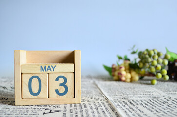 May 3, Calendar cover design with number cube with fruit on newspaper fabric and blue background.