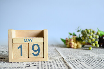 May 19, Calendar cover design with number cube with fruit on newspaper fabric and blue background.