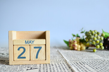 May 27, Calendar cover design with number cube with fruit on newspaper fabric and blue background.