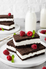 Chocolate cake with milk cream filling on a white plate with fresh raspberries and mint with...