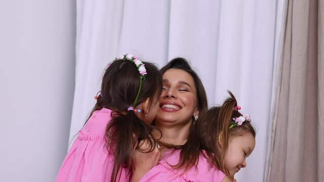 mother and 2 girls in bedroom, kissing and hugging eachother.mom and daughters jumping on mattress.kids and woman in pink dresses,many flowers on floor.international mother women day.vertical video