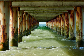 Rusty pillars of old sea pier create mesmerizing seascape scene with view from under pier, restless...