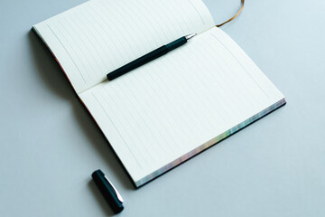 flatley photo. a gray open notebook with a leather cover and a black pen on a light plain...