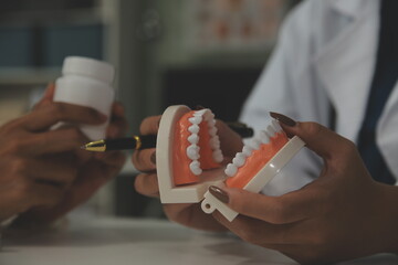 Concentrated dentist sitting at table with jaw samples tooth model and working with tablet and...