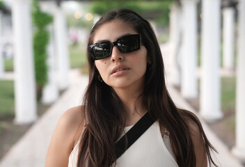 Portrait of a young latin american woman wearing sunglasses, in the park with a beautiful sunset...