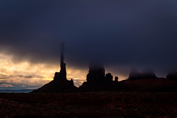 Totem Pole in Monument Valley during morning storm shows an eerie scene as the black clouds block the setting sun.