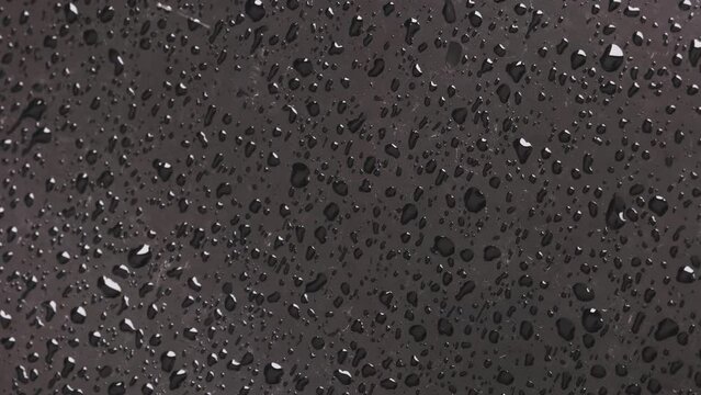 rain drops on black car bonnet surface, closeup with slow motion