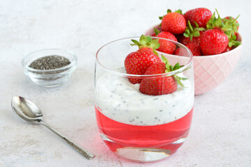 a glass of yogurt with strawberries and a spoon next to it