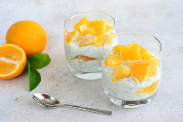 two glasses of yogurt with oranges and a spoon next to them 