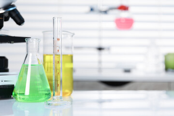 Laboratory analysis. Different glassware with liquids and microscope on white table indoors, space for text