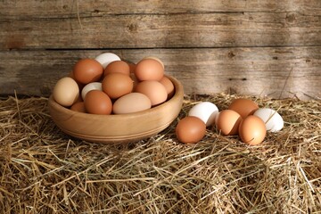 Fresh chicken eggs on dried straw bale near wooden wall