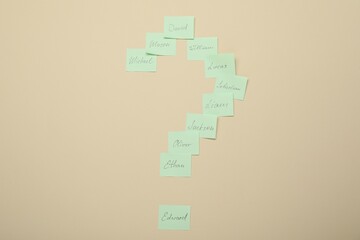 Choosing baby`s name. Paper stickers with different names in shape of question mark on beige background, top view