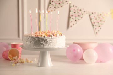 Tasty Birthday cake with burning candles and party decor on white table, space for text
