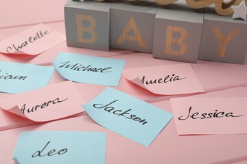 Cubes with word Baby and paper stickers with different names on pink wooden table. Choosing baby's...