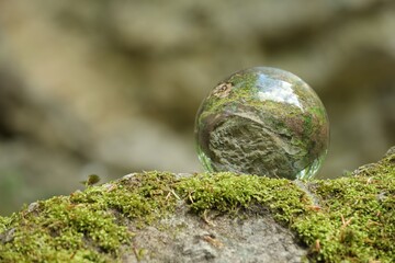 Beautiful forest, overturned reflection. Crystal ball on stone surface with moss outdoors. Space for text