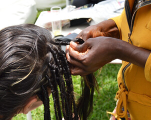 Gros plan des mains du coiffeuse faisant des tresses africaines dans les cheveux d'une jeune femme...