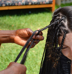 Mani di un parrucchiere africano che fa trecce nei capelli di una giovane donna all'aperto in vacanza al mare. Primo piano dell'intrecciatura dei capelli