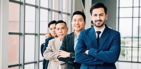 A united group portrait captures young businesspeople and a businessman confidently standing in the office with crossed arms. Their dedication to success and teamwork is evident.