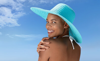 Portrait of a woman wearing a blue sun hat on the hot summer beach, enjoying a holiday by the sea....