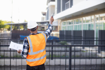 Behind the scenes foreman wearing reflective vest and hard hat inspects construction site to ensure...