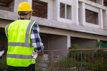 Behind the scenes foreman wearing reflective vest and hard hat inspects construction site to ensure...