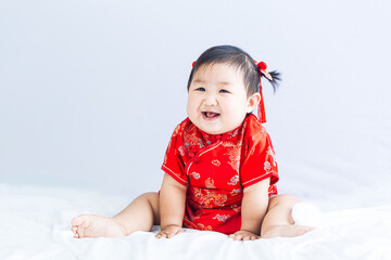 Chinese New Year concept, cute happy little girl in Chinese dress sitting in white living room. Cute Asian baby sitting in white living room, Chinese New Year concept.