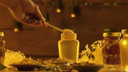 Glass jars standing on the wooden table with fresh golden honey, man taking honey dipper and pours...
