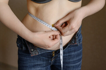 Woman measures her fat belly with a tape measure on a gray background, close-up. Problem of excess...