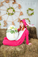 Beautiful redhaired woman wearing bunny costume with big egg sitting on the haystack Easter holiday concept