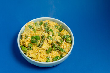 A traditional Alentejo dish, featuring scrambled eggs mixed with vibrant green asparagus. The golden hues of the eggs contrast beautifully with the deep blue background.