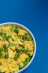 A traditional Alentejo dish, featuring scrambled eggs mixed with vibrant green asparagus. The golden hues of the eggs contrast beautifully with the deep blue background.